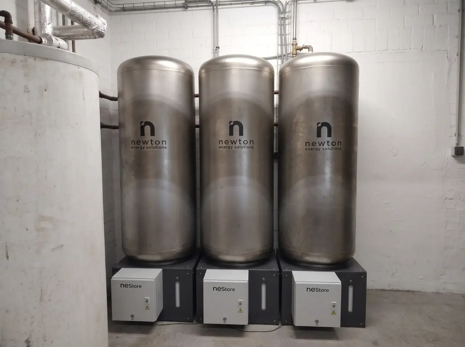 Newton NEStore-waterbatterijen: drie gelijke roestvrijstalen tanks op een zwarte sokkel in een technische ruimte